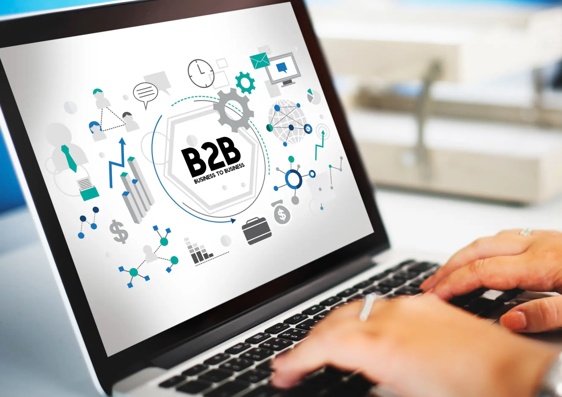 A person typing on a laptop displaying a B2B graphic with business icons, emphasizing business-to-business concepts and analytics
